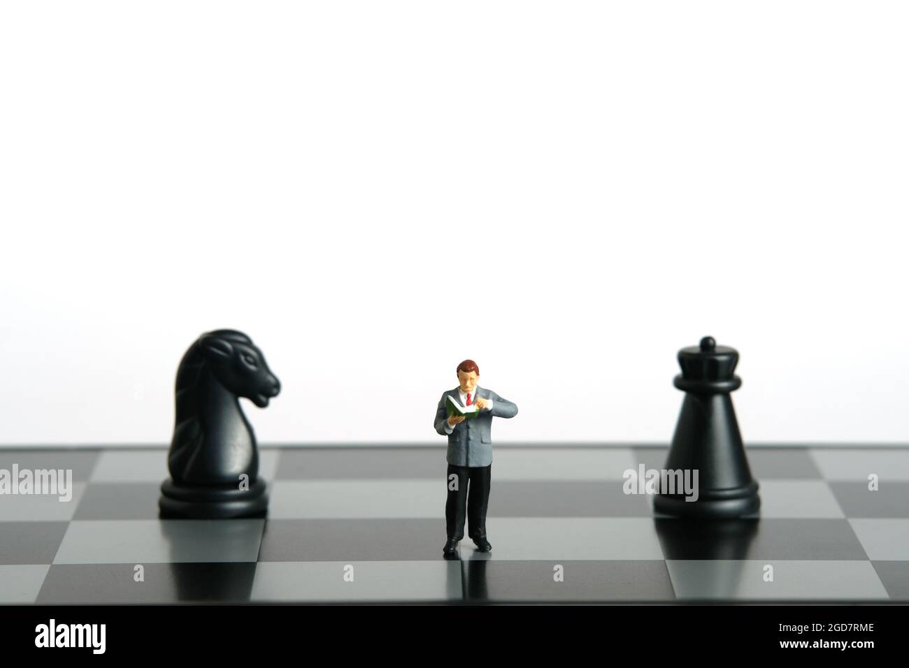 Miniature people toy figure photography. Defensive or attack strategies concept. A men student standing in between horse and castle chessboard pawn kn Stock Photo