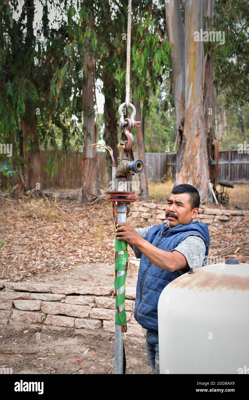 Two men pulling a water well pump and replacing the 20 foot pipe which was 26 years old - ethnic Hispanic, did the 180 foot job in a day. Stock Photo