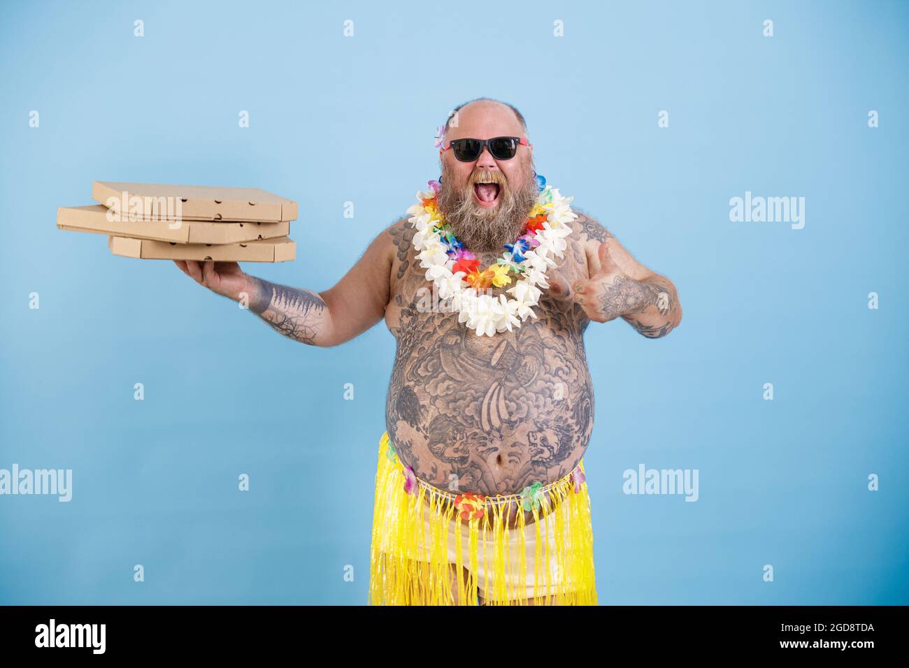 Joyful obese man with flowers garland holds boxes of pizza on light blue background Stock Photo