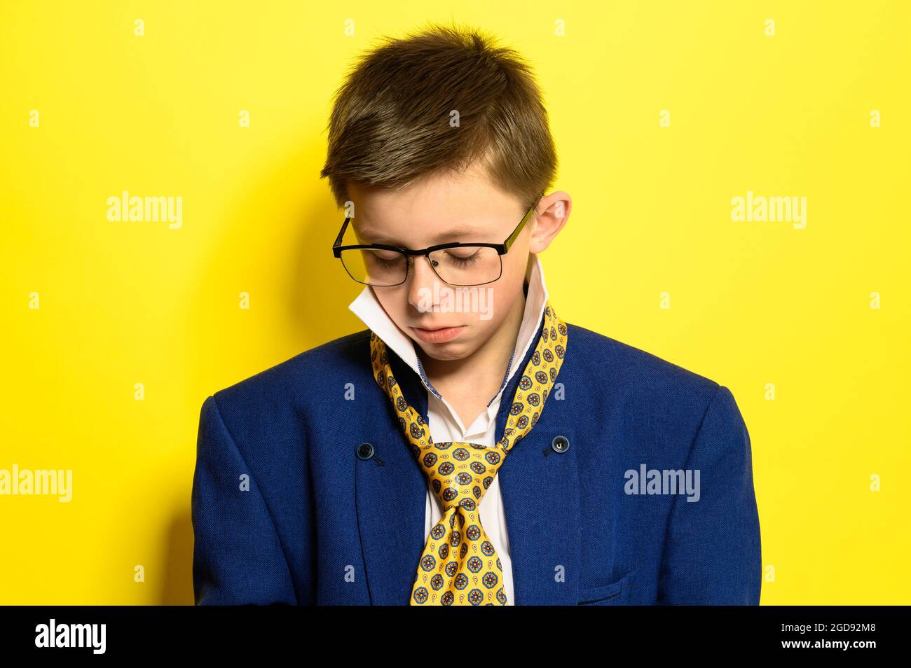 Portrait of a boy on a yellow background with a sad expression, an adult suit on a child. new Stock Photo