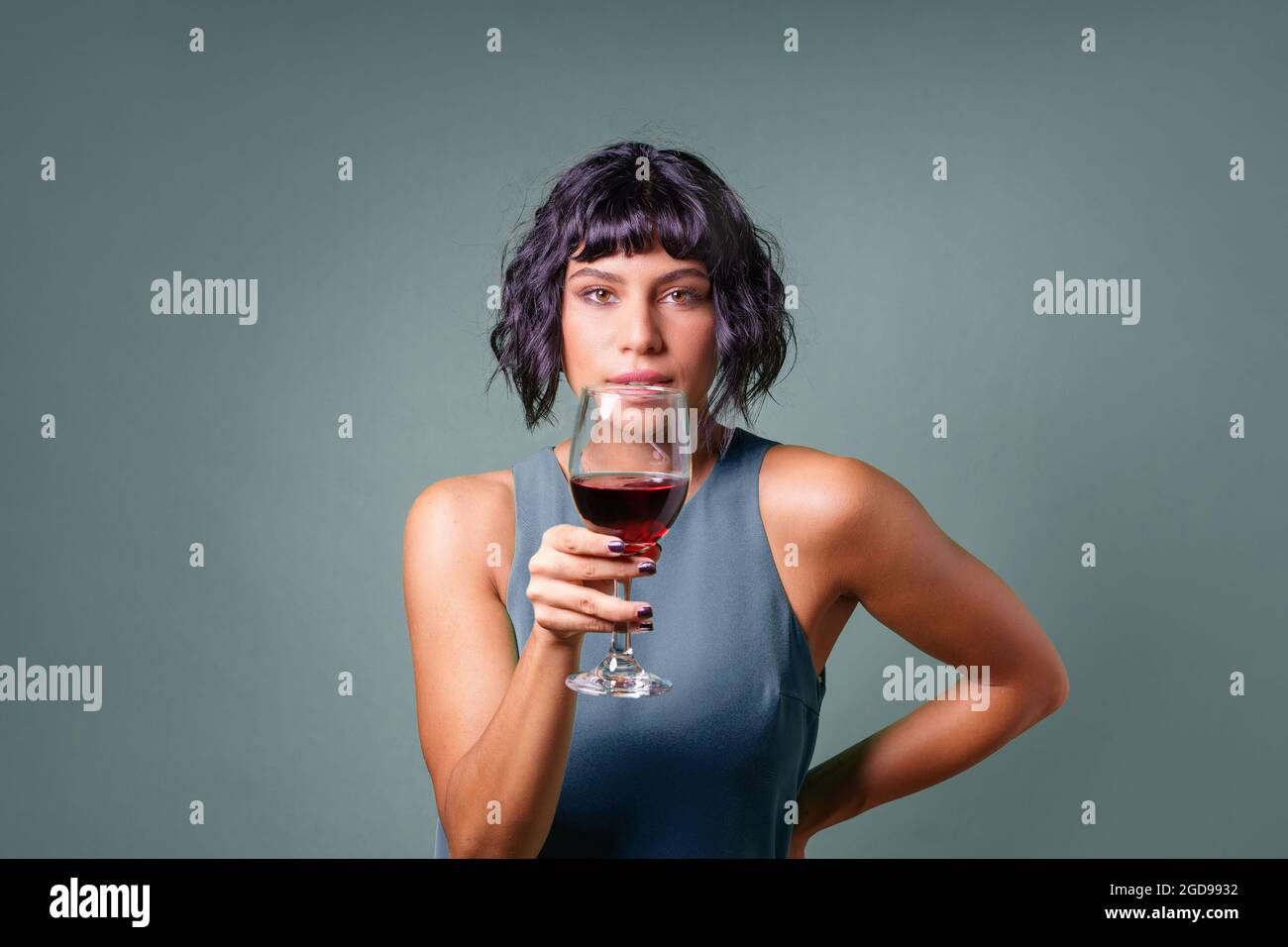 Young woman holding a red wine glass watching the camera. Isolated on a ...