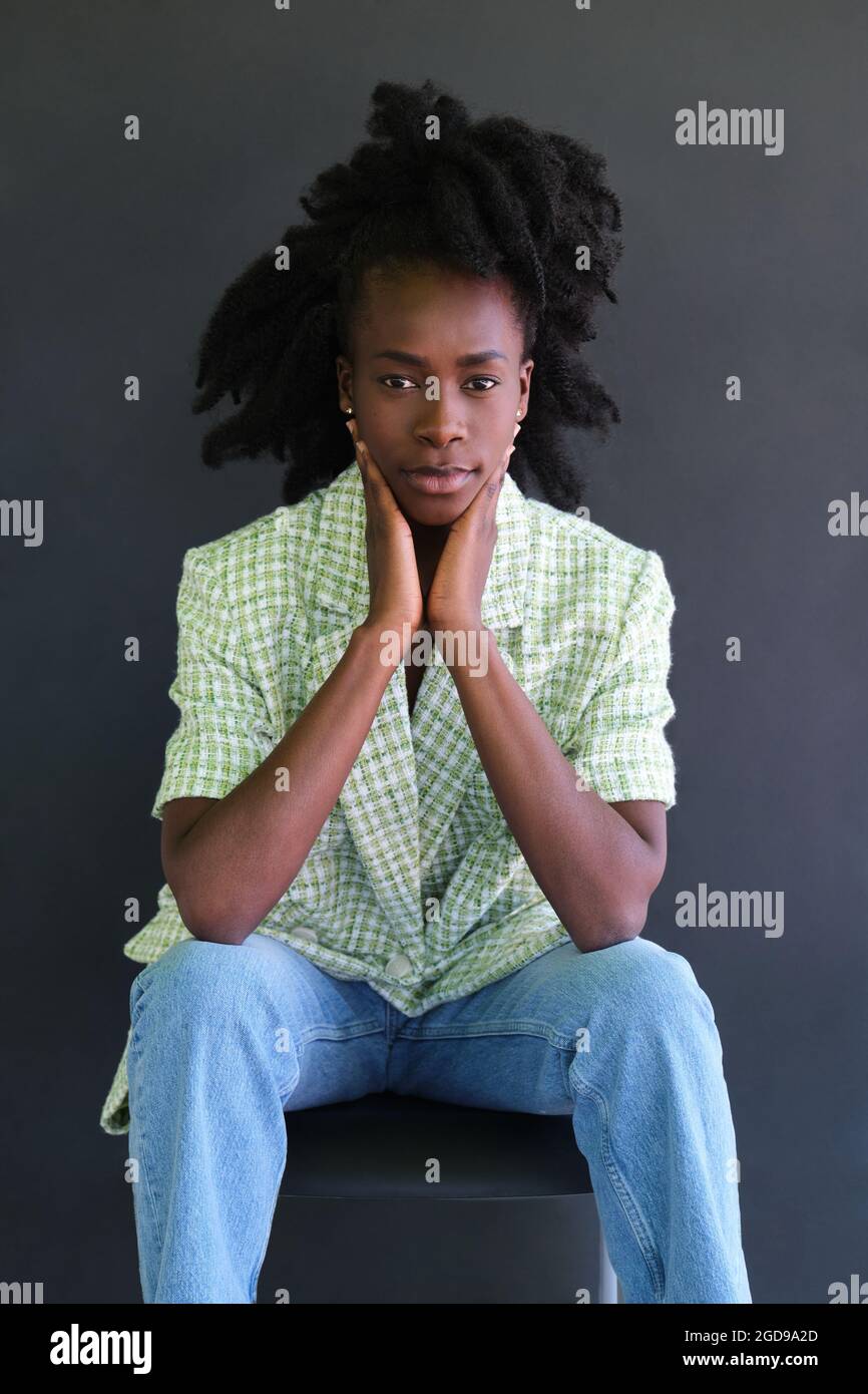 Portrait of an african young woman sitting on a chair wearing green ...