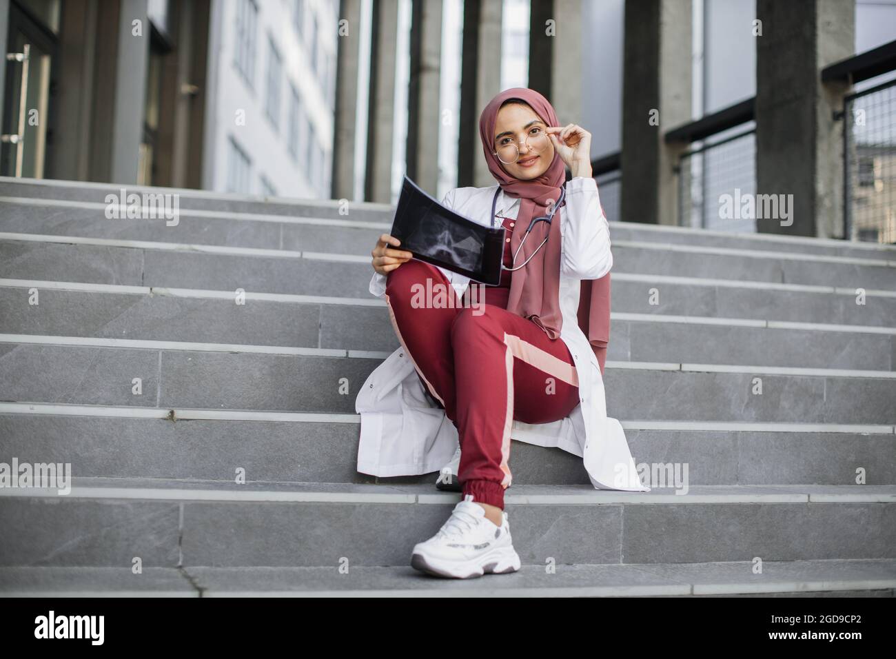 Pretty muslim asian female medical doctor, wearing hijab, red scrubs