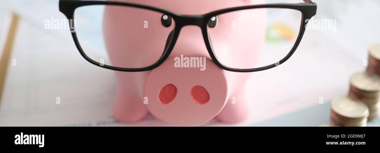 Pink piggy bank with glasses standing near heaps of coins and ...