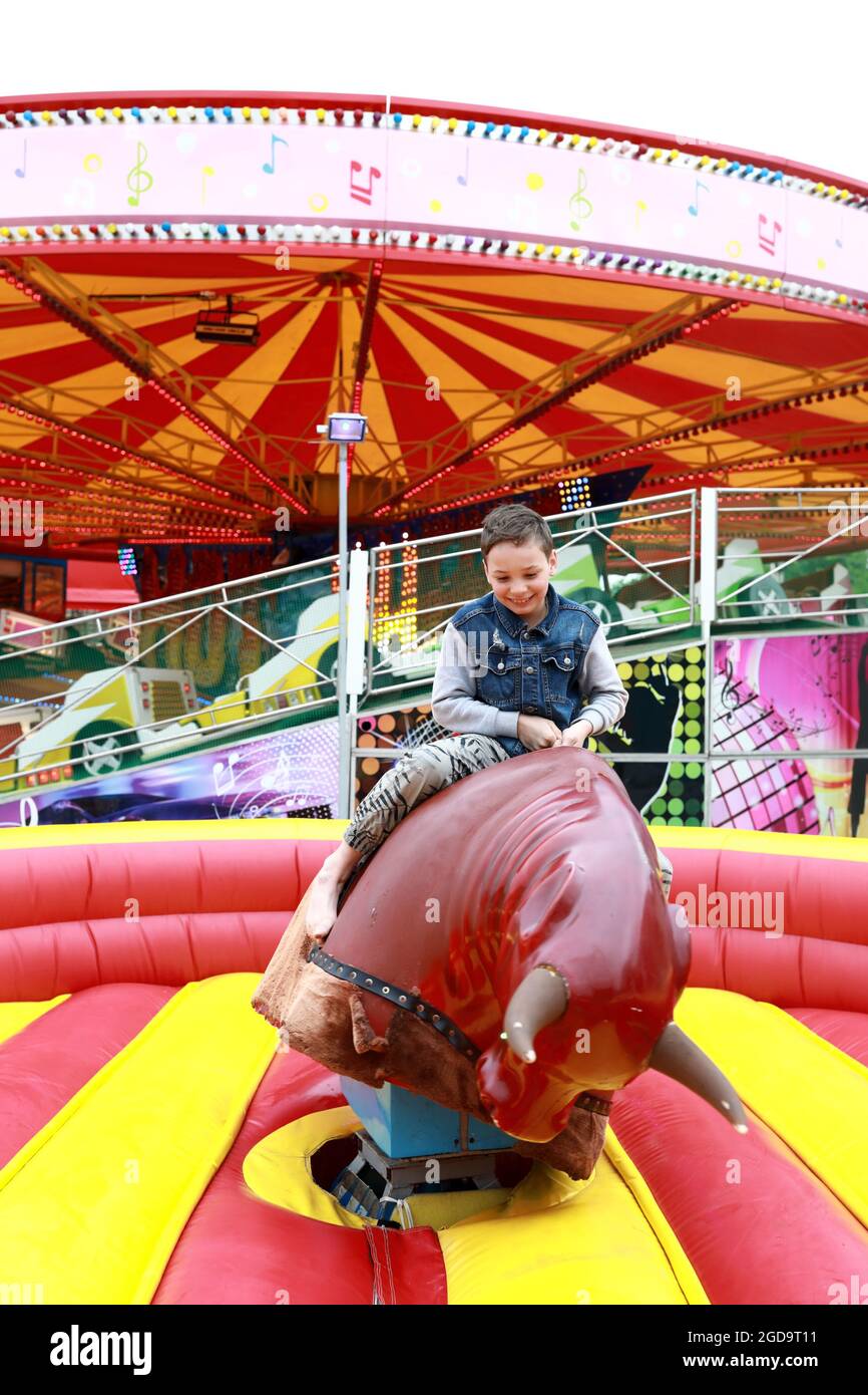 Kid riding on mechanical bull in amusement park Stock Photo