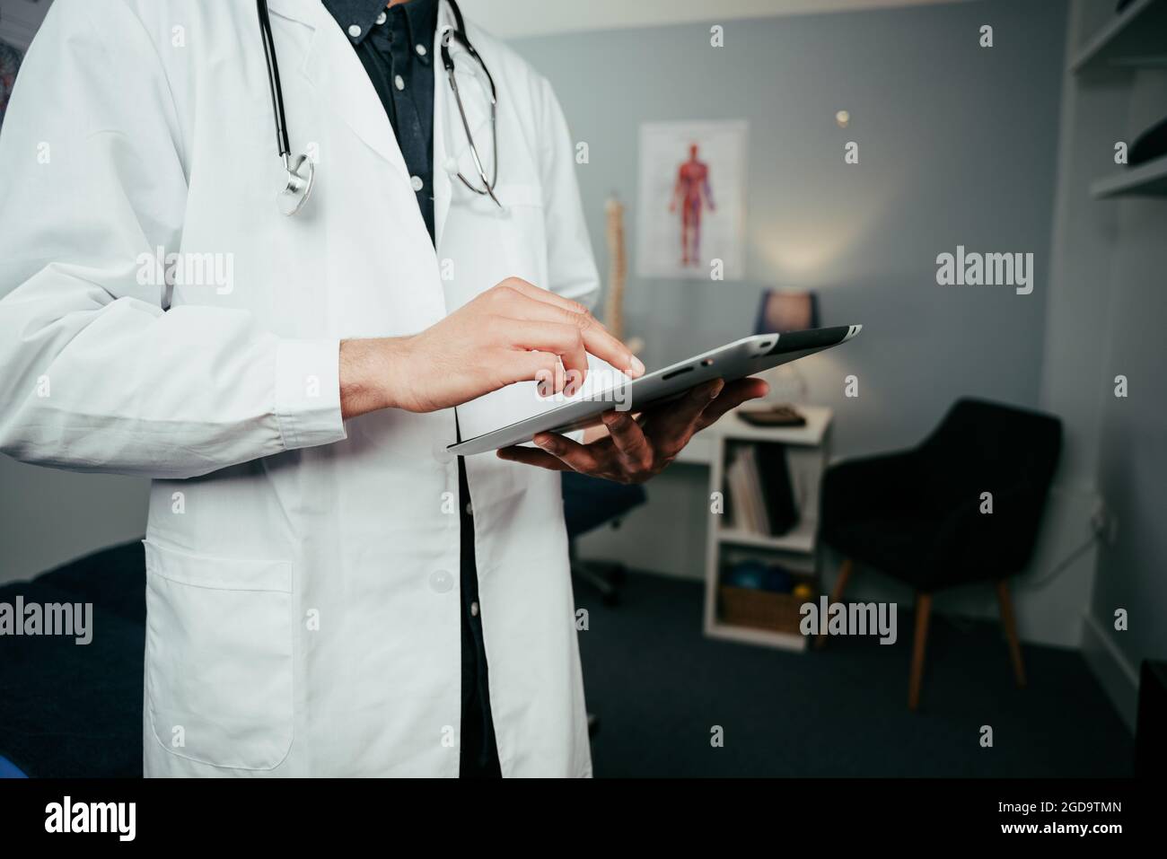 Male nurse standing in clinic typing on digital tablet  Stock Photo