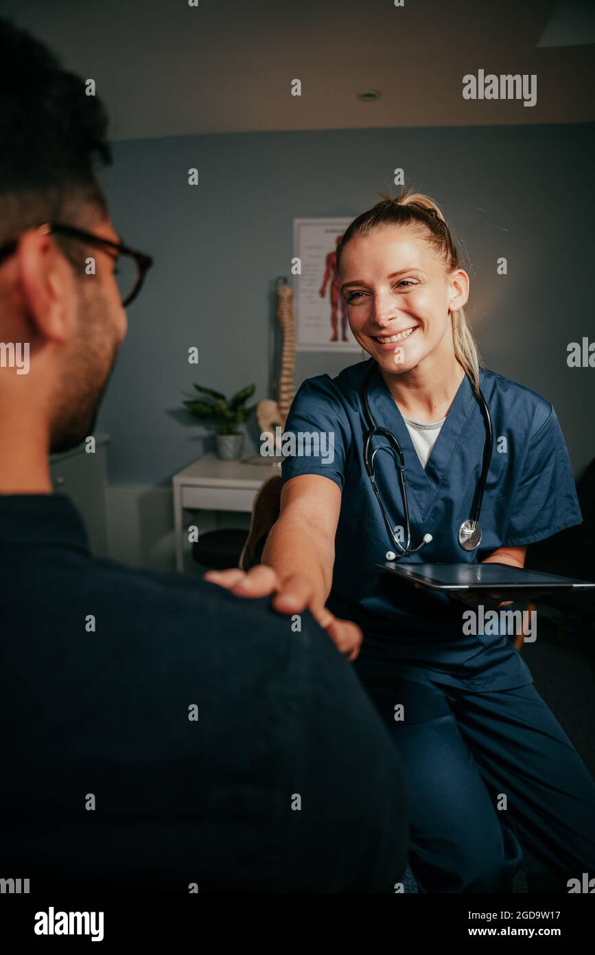 Caucasian female nurse standing in clinic chatting to male patient Stock Photo
