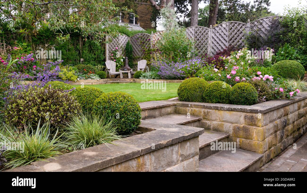 Colourful landscaped private garden in summer (contemporary design, terracing & terrace, raised beds, patio seats, lawn, ) - Yorkshire, England, UK. Stock Photo