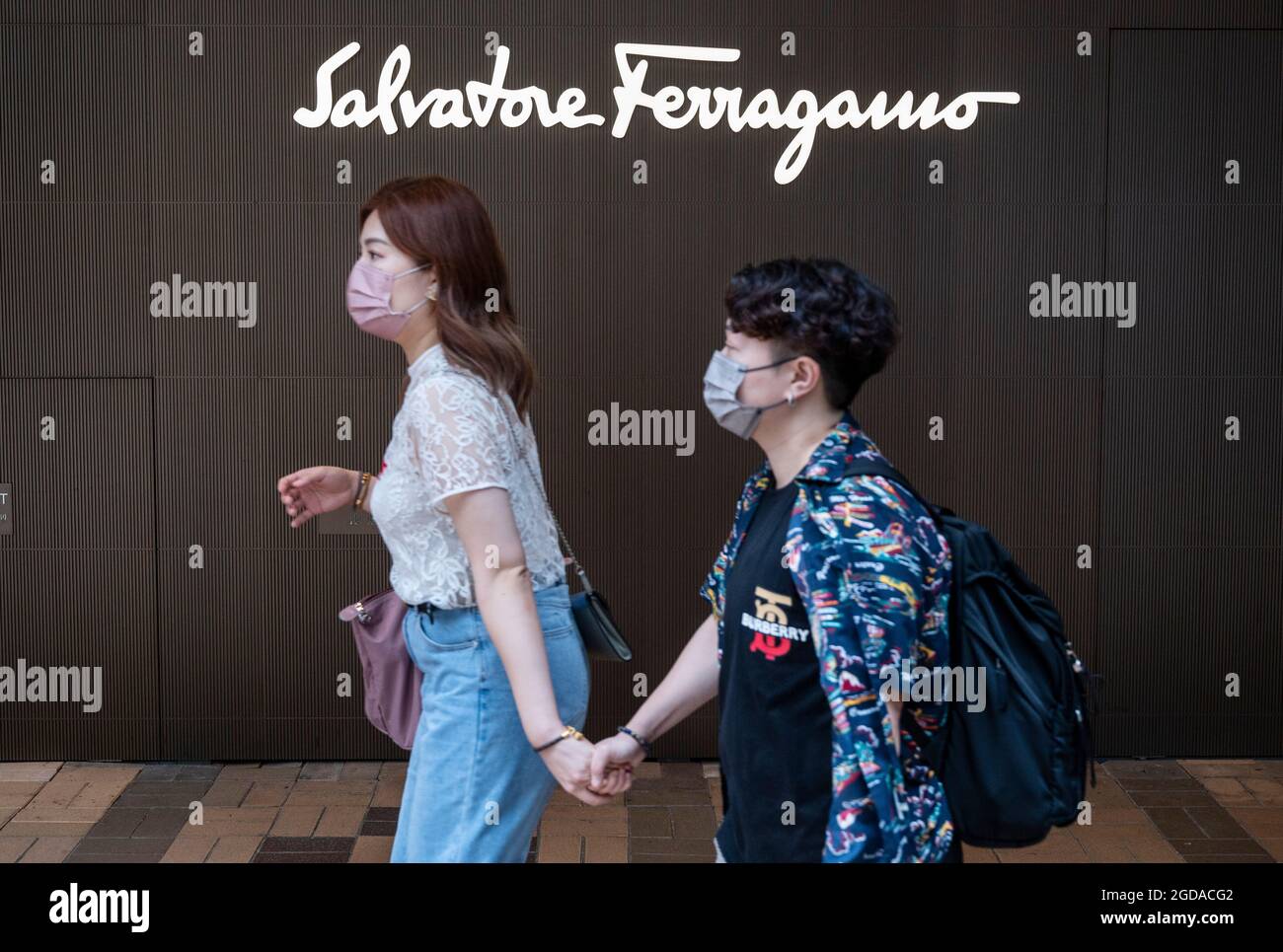 Pedestrians walk past the Italian luxury shoe brand Salvatore Ferragamo store and logo seen in Hong Kong. Stock Photo