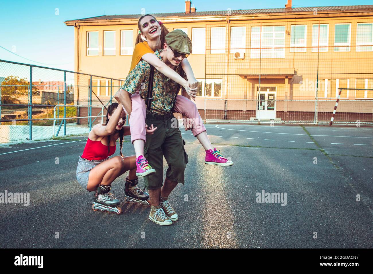 Group of friends hanging out outside. One girl back riding her friend, other rides behind on rollers. Positive vibes Stock Photo