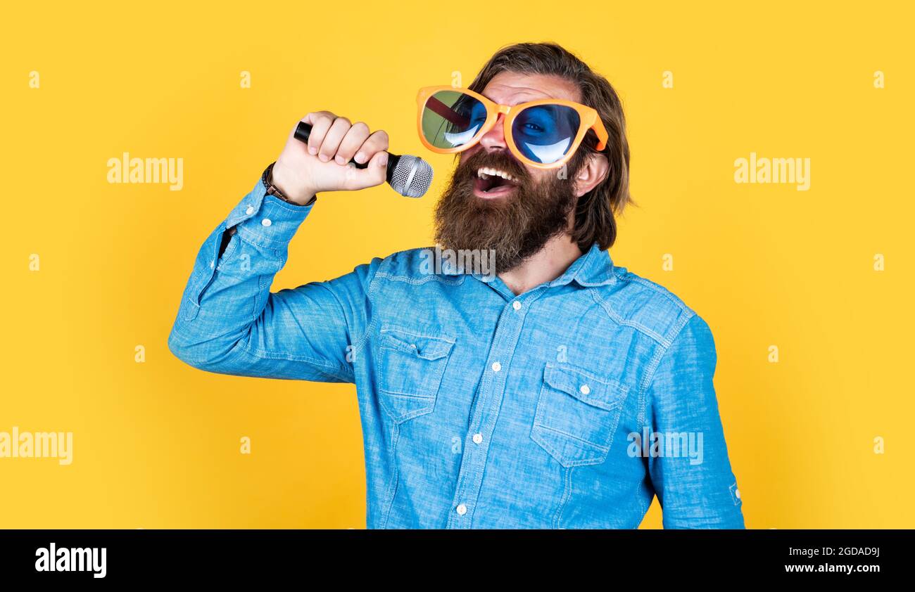 he is talanted. guy with beard sing in microphone. brutal caucasian hipster event manager. funny party glasses. karaoke and music. male speaker with Stock Photo