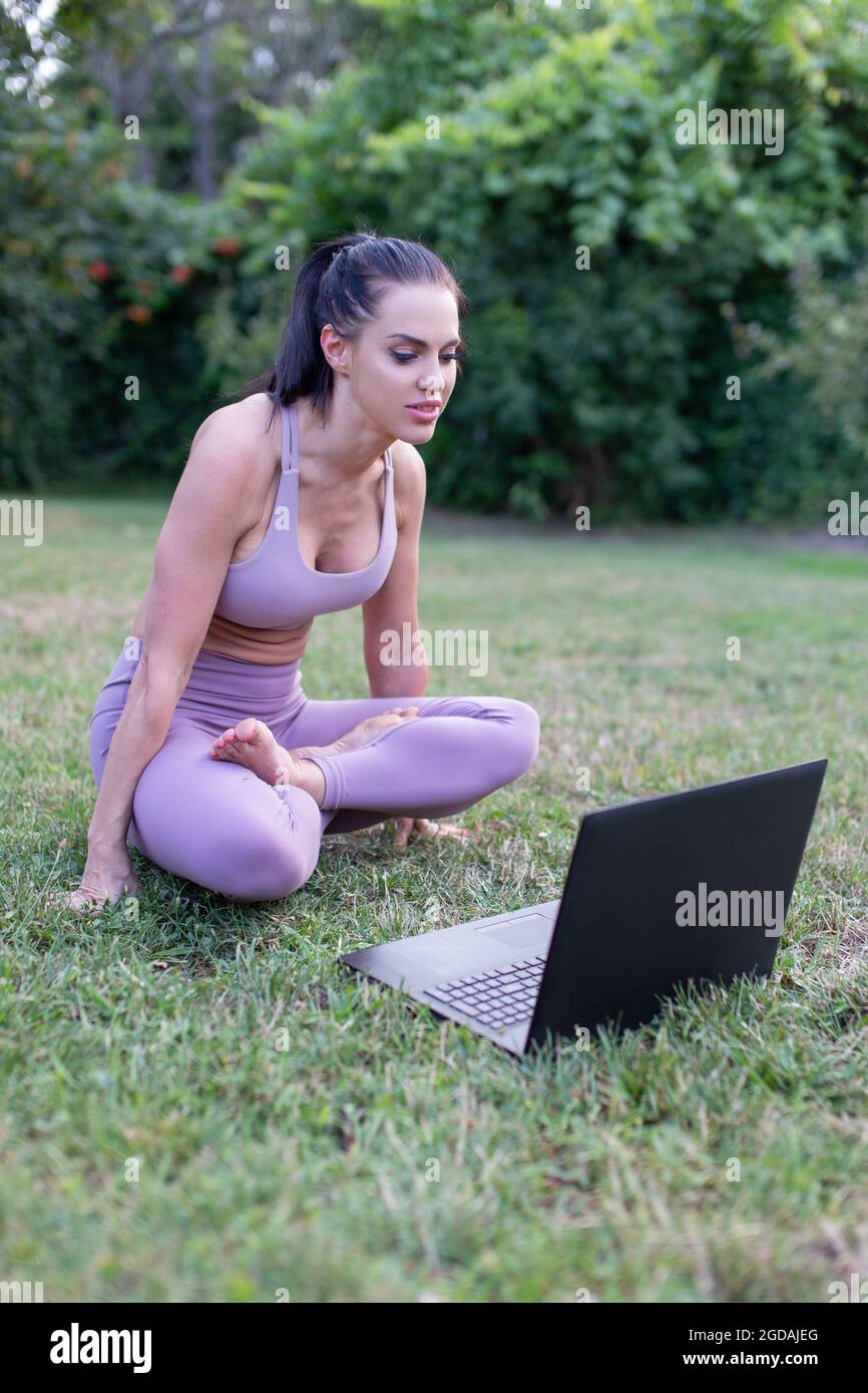 Young woman in sportswear learning from tutorial video,  handstand lotus sit yoga pose in garden, outdoors Stock Photo