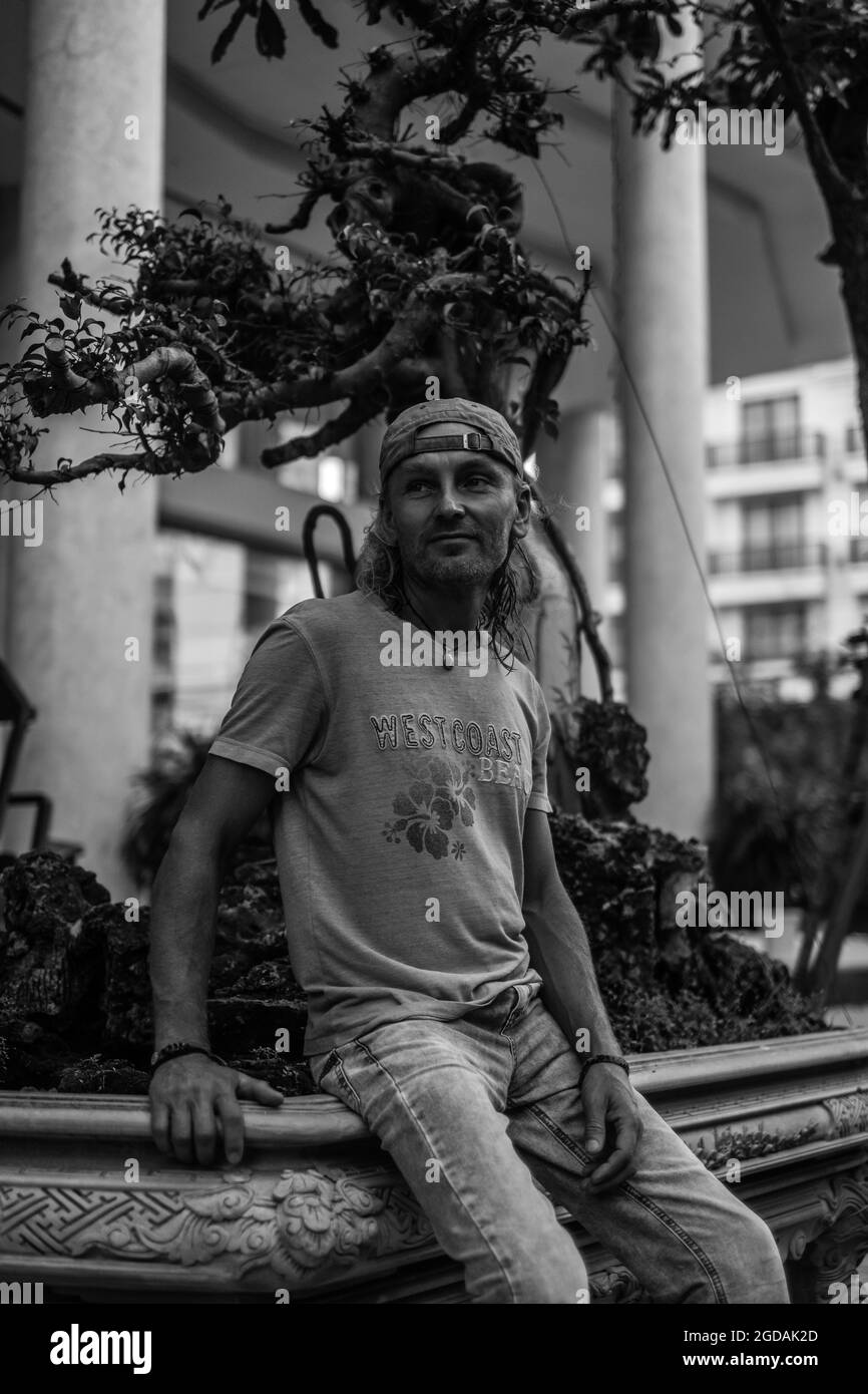 Mature man in t-shirt, jeans and cap sitting on the street in town. Black and white photo. High quality photo Stock Photo