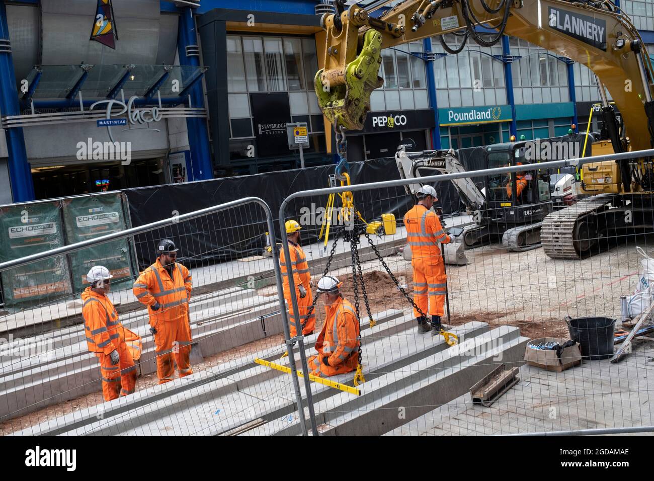 Team of workmen wearing orange high-viz overalls on a construction site work at laying the new track foundations for the update to the Midland Metro tram public transport system in the city centre along Corporation Street on 3rd August 2021 in Birmingham, United Kingdom. The original tracks are being pulled up and relaid, while a new line is also under construction and due to open later in the year. The Midland Metro is a light-rail tram line in the county of West Midlands, England, operating between the cities of Birmingham and Wolverhampton via the towns of West Bromwich and Wednesbury. The Stock Photo