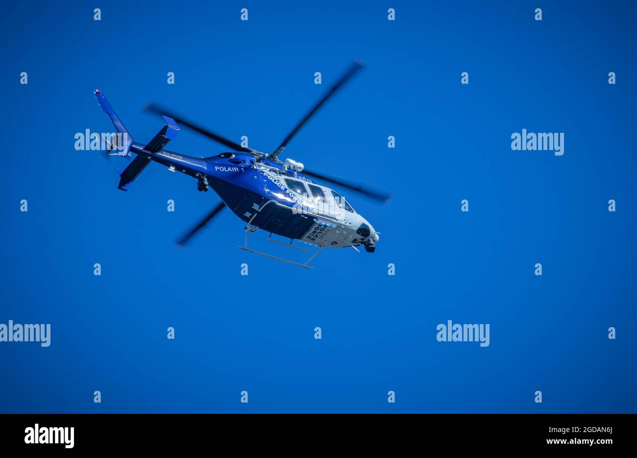 New South Wales Police Force, Polair 1, Police helicopter flying high against a blue sky with motion blurred rotor blades, sun reflecting Stock Photo