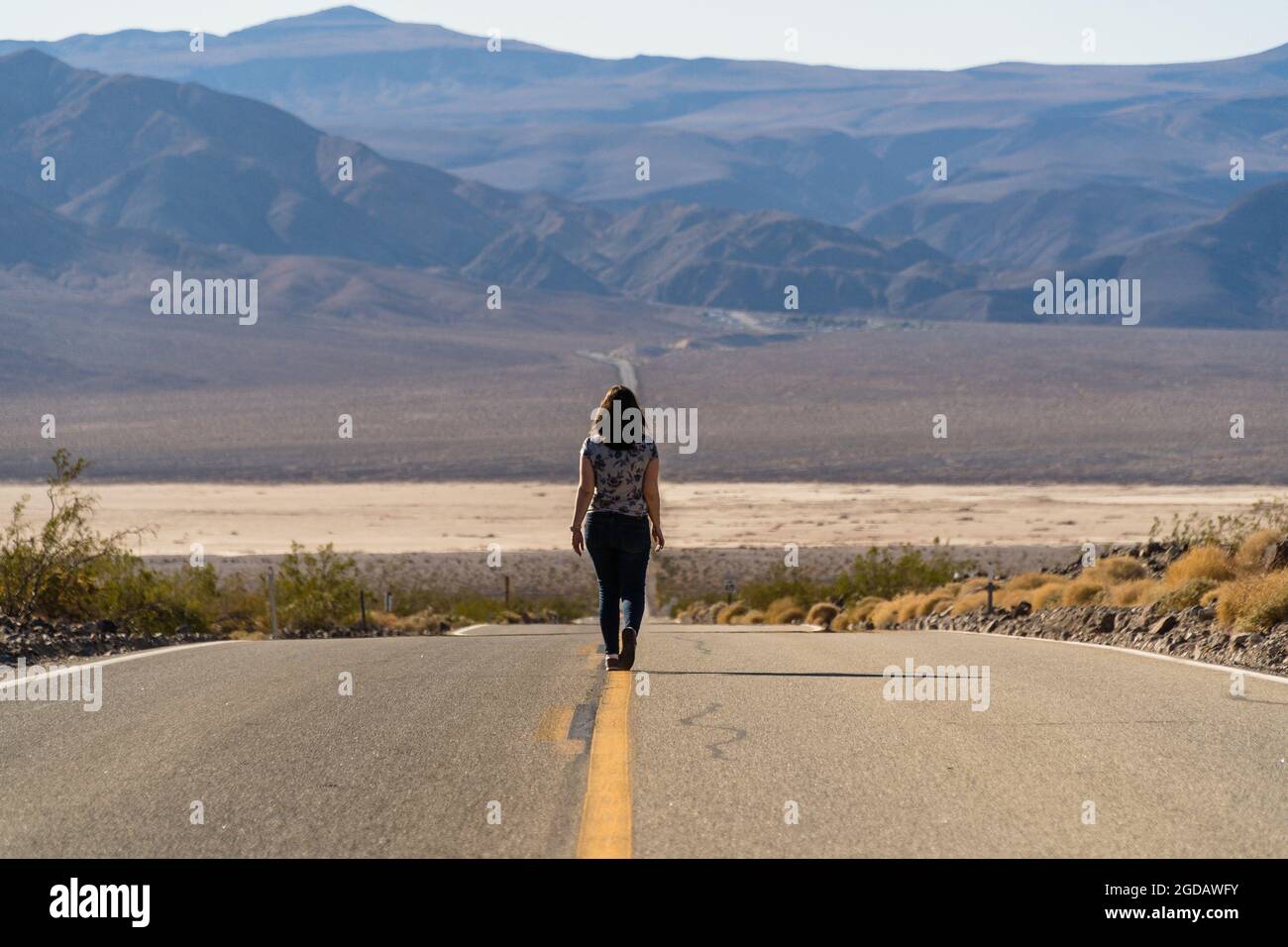 Female walking on the asphalt road looking at mountains in the USA ...