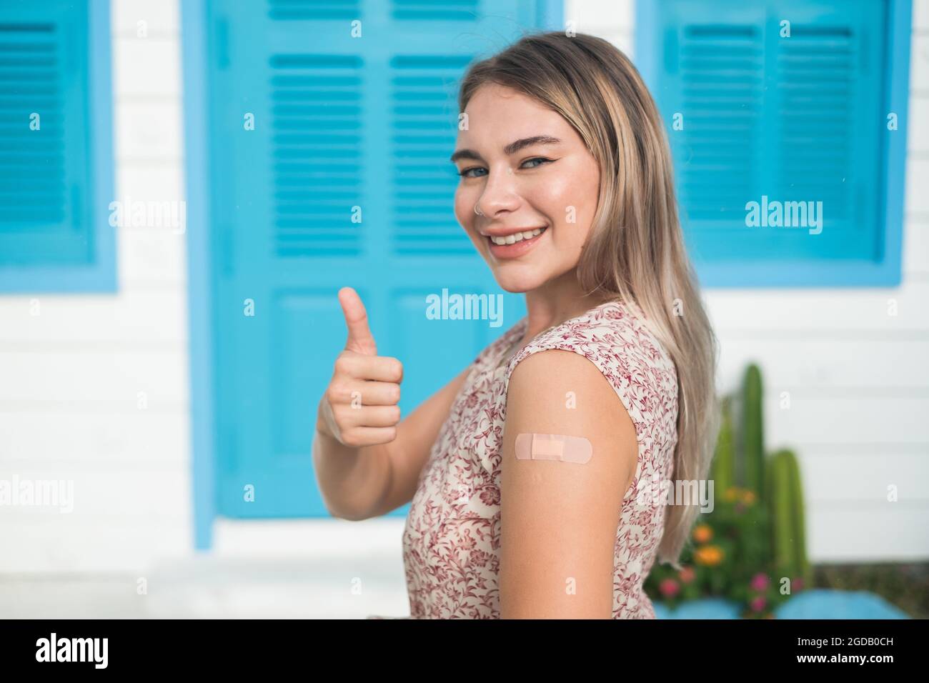 Vaccinated caucasian young woman with blond hair showing thumb up and looking at camera with copy space. Covid-19 or coronavirus vaccine. Vaccination Stock Photo