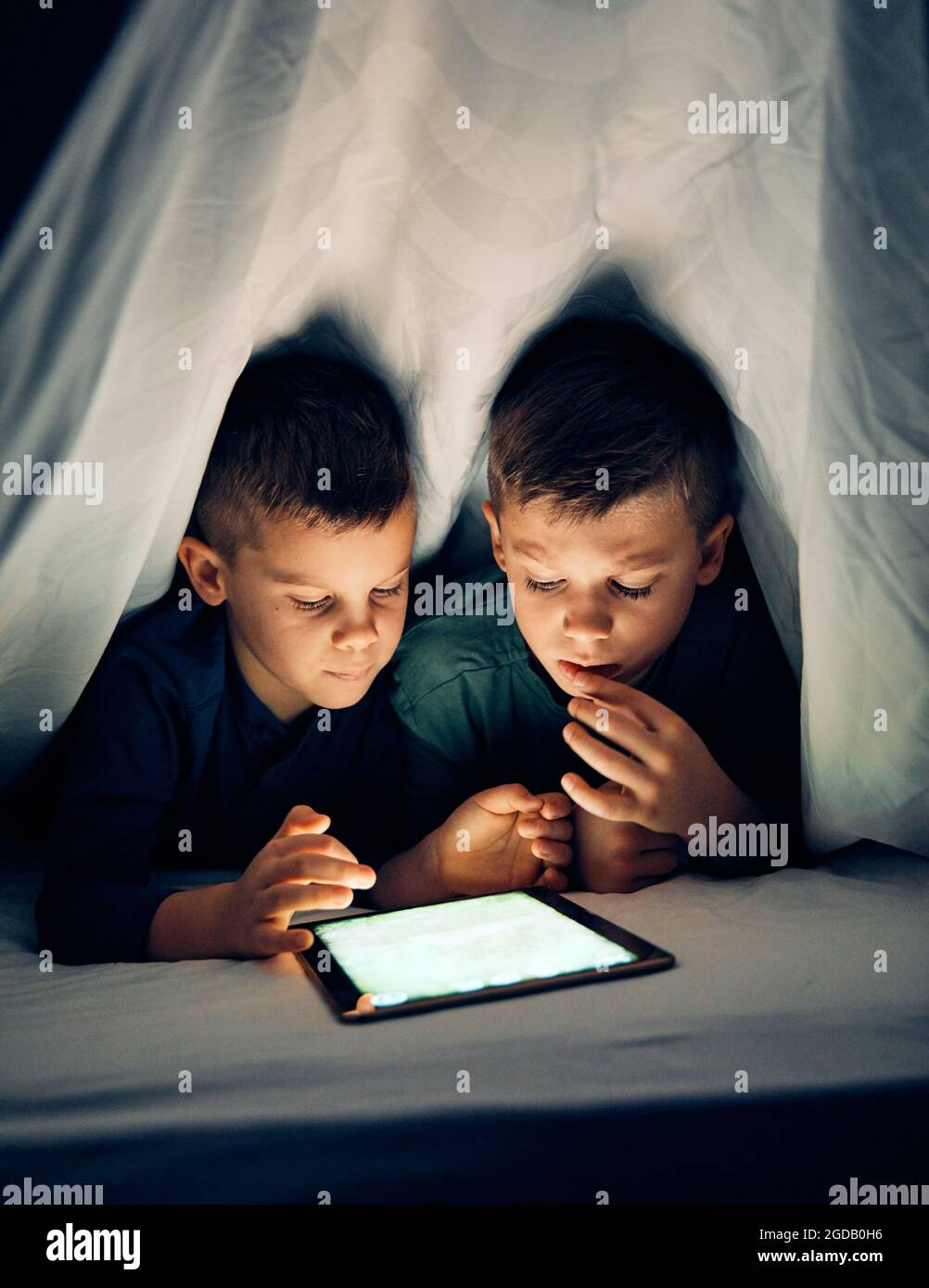 child brother friend having fun tablet laptop under sheet bedtime kid Stock Photo