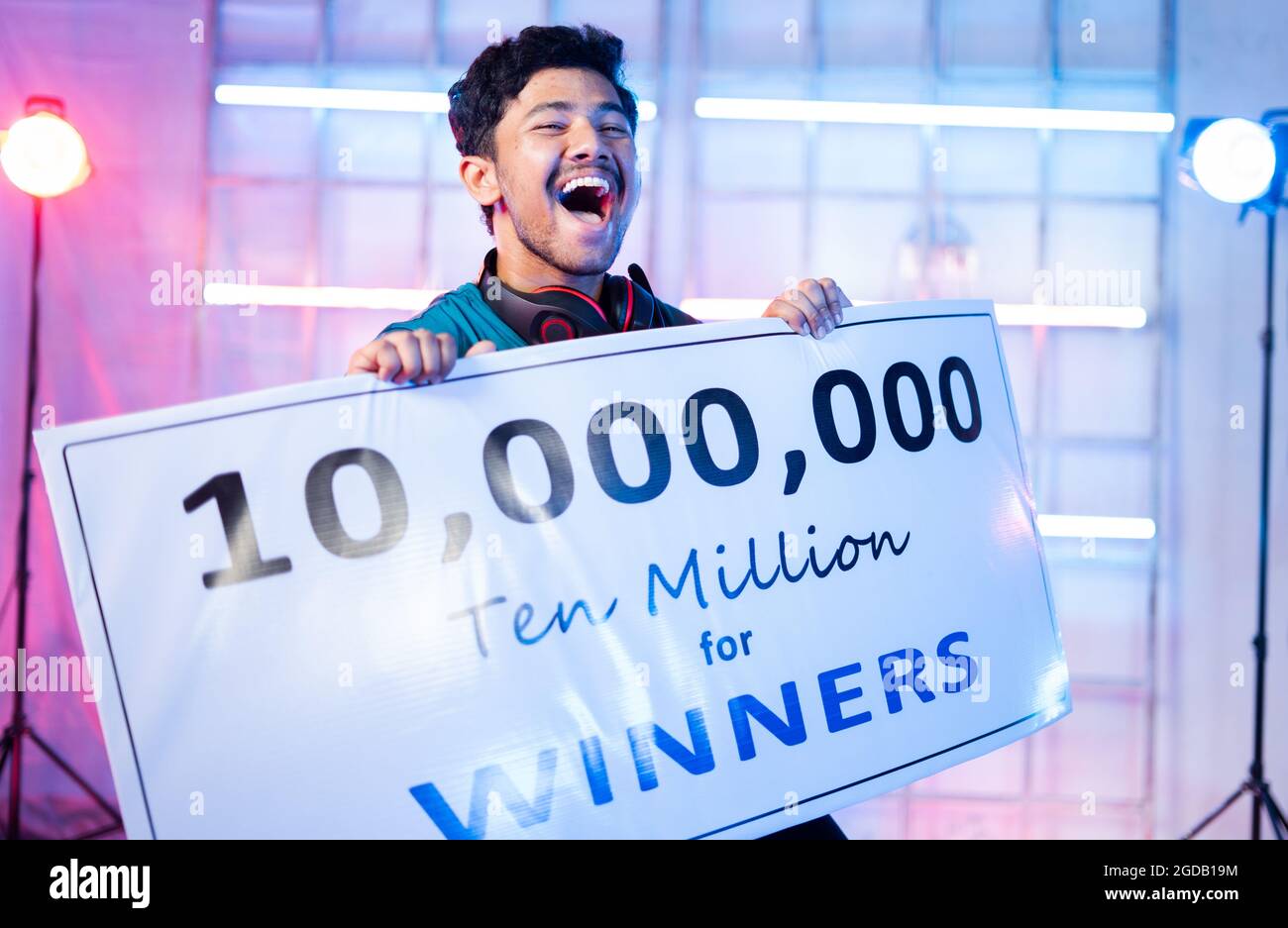 Excited Professional esports gamer with headphones celebrating and dancing by holding winners price money presentation at video gaming tournament on Stock Photo