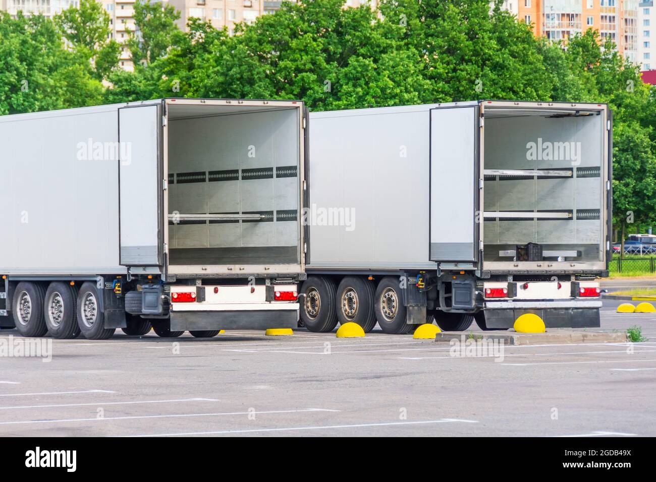 Two trucks in a parking lot with an empty container trailer open gates ...