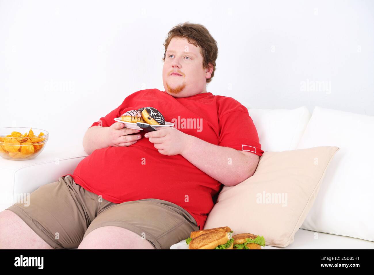 Lazy overweight male sitting with fast food on couch and watching