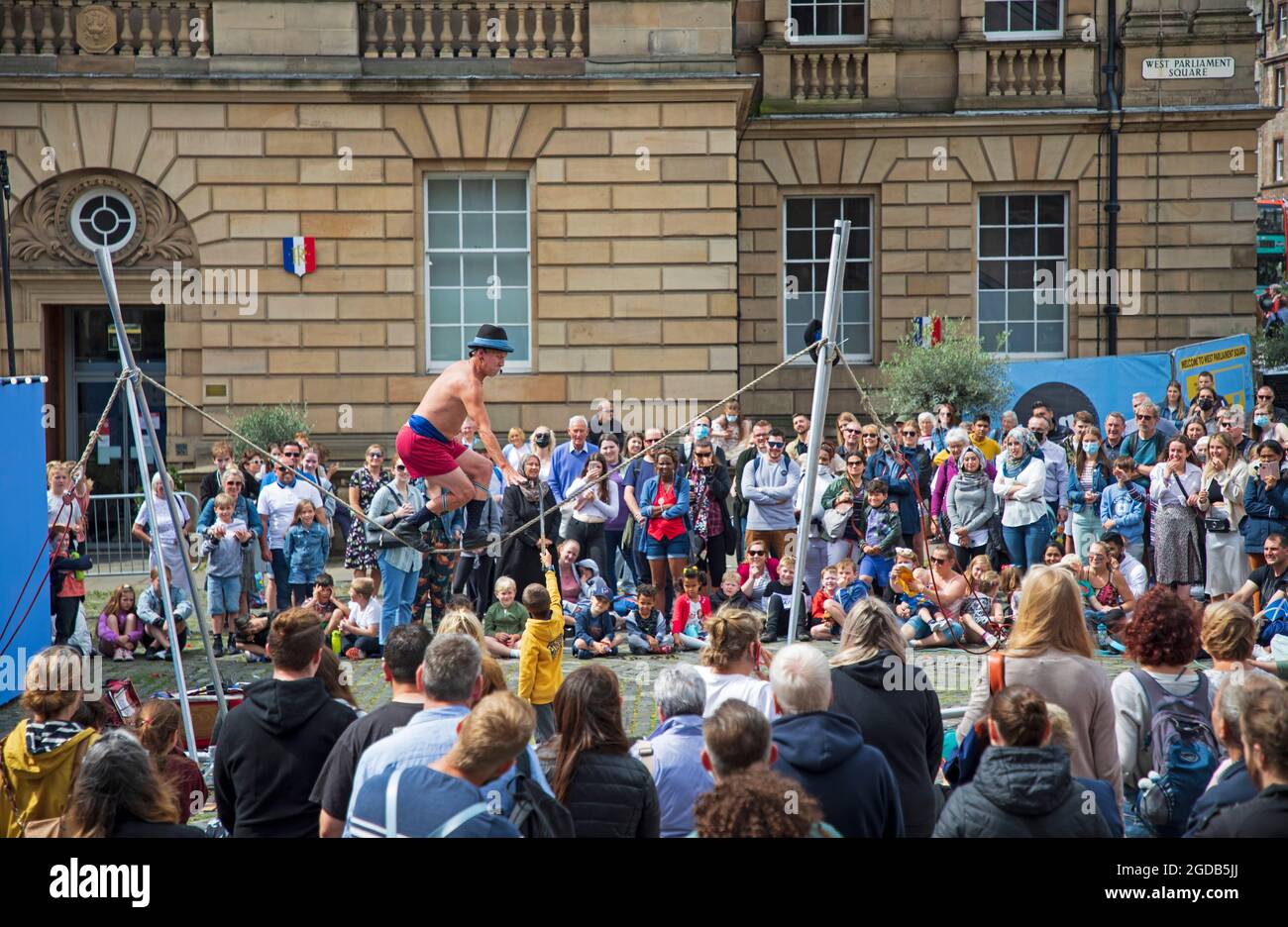 Royal Mile, Edinburgh, Scotland, UK. 12th Aug, 2021. Edinburgh Fringe Festival, day seven of the goings on on the capital city High Street event. Weather breezy and cloudy with temperature of 18 degrees for the human statues and street performers drawing crowds to their pitches. Pictured: Kwabana Lindsay entertains a large audience on Parliamnet Square. Credit: Arch White/Alamy Live News Stock Photo