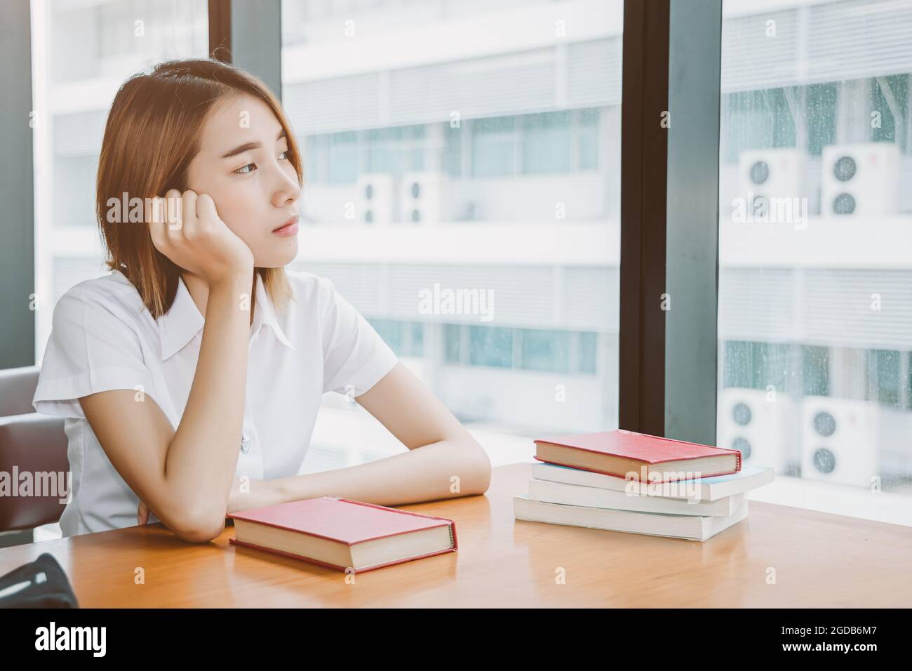 Asian university girl teen sitting alone thinking worry, day dreaming or boring looking out window lonely expression in library. Stock Photo