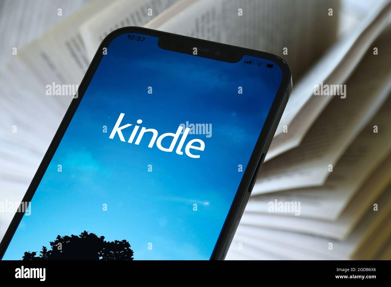 Amazon Kindle mobile app on cellular phone. Download and read digital ebooks in app. E-reader on mobile in front of open paperback. Stock Photo