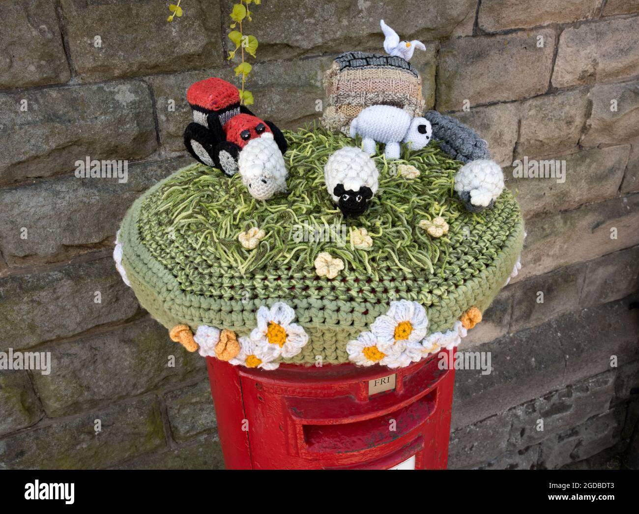 A knitted rural farm scene 'hat' on the top of a post box in Hawes, in the Yorkshire Dales National Park, UK. Stock Photo