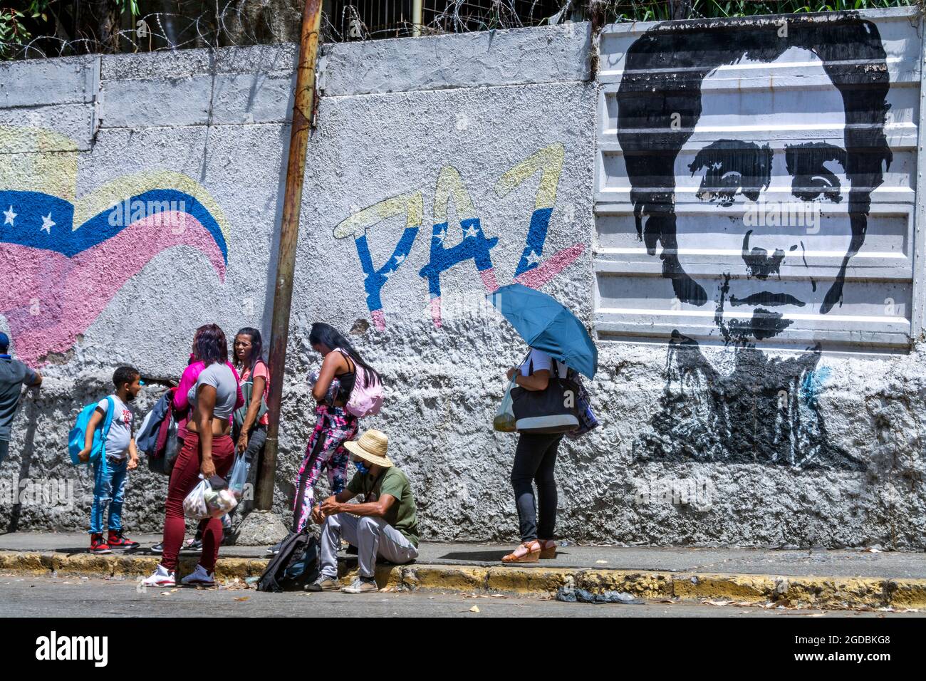 A group of people wait for a bus in the Las Mayas neighborhood in Caracas, Venezuela; in the back a mural with the face of the liberator Simon Bolivar Stock Photo