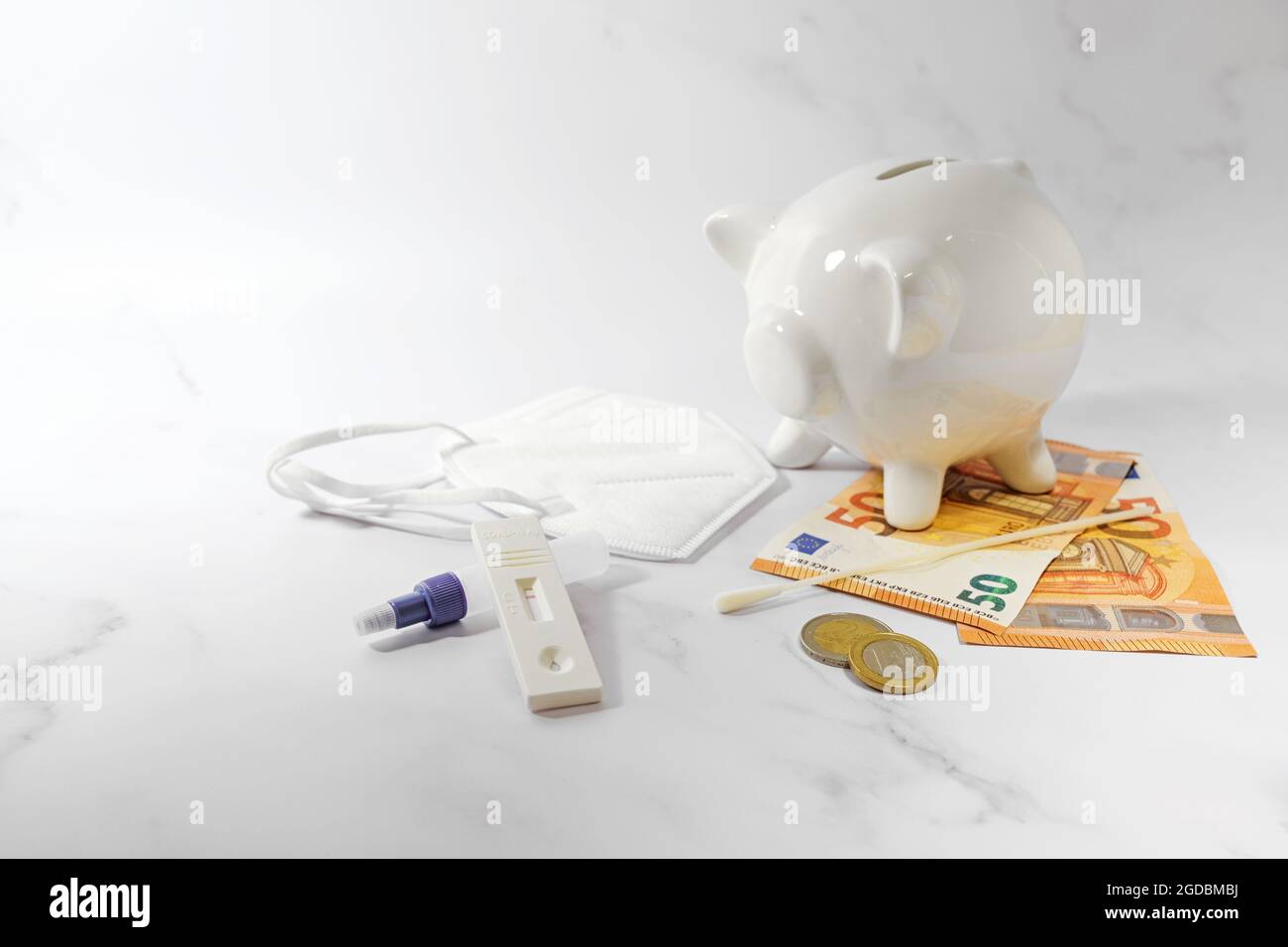 Covid-19 rapid test kit, euro notes and coins, piggy bank and a ffp2 face mask on a gray background, concept for health care costs during coronavirus Stock Photo