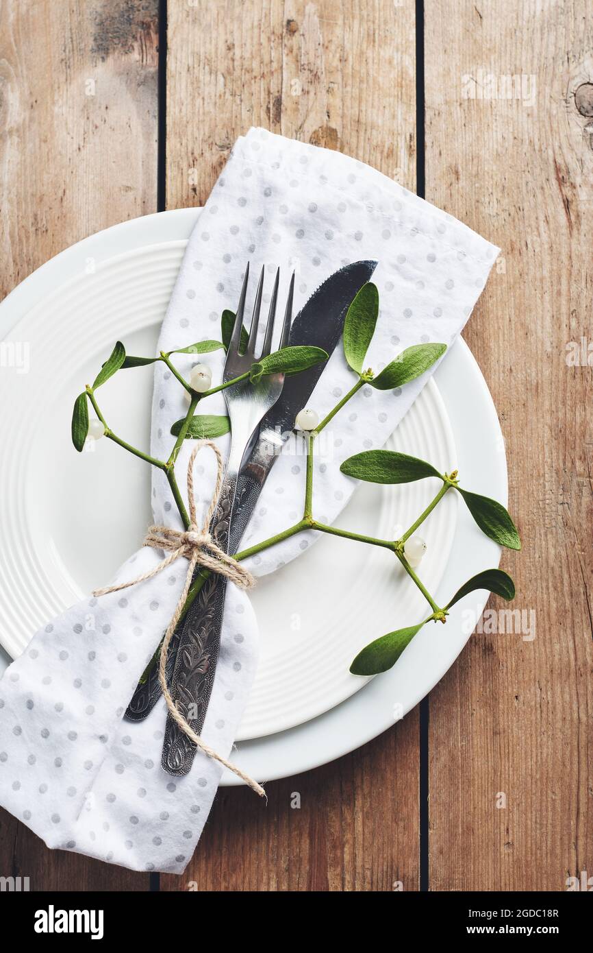 Table setting. White plates, cutlery, napkin and mistletoe. Stock Photo