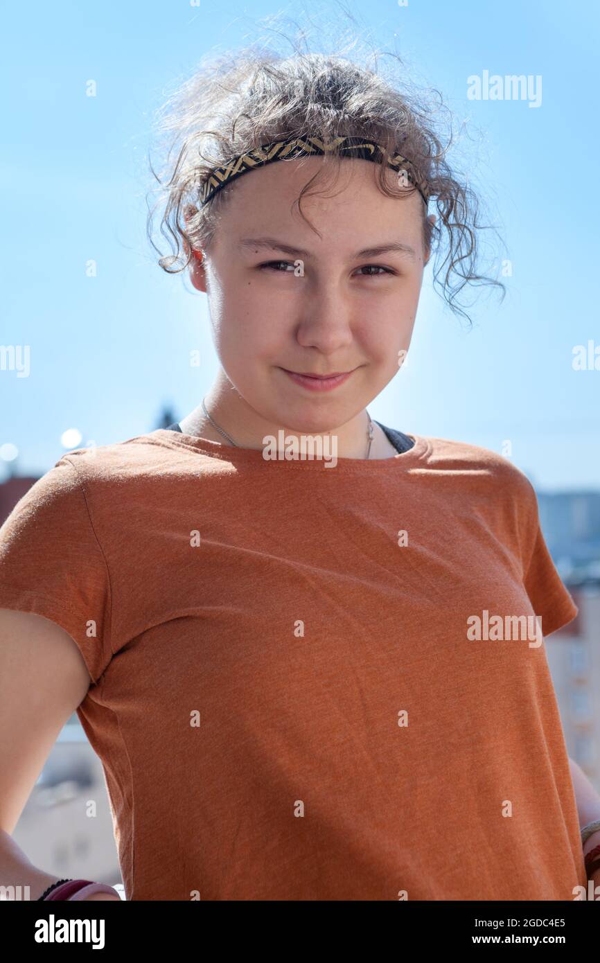 Curly hair teen girl portrait, girl wearing red t-shirt looking at camera and smiling, Caucasian person Stock Photo