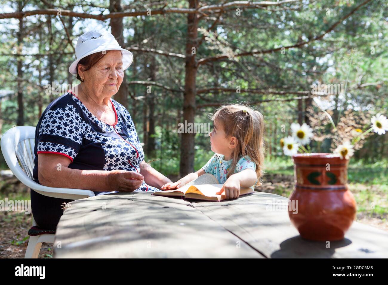Granddaughter smell flowers with her senior granny, women sitting in forest and talking Stock Photo