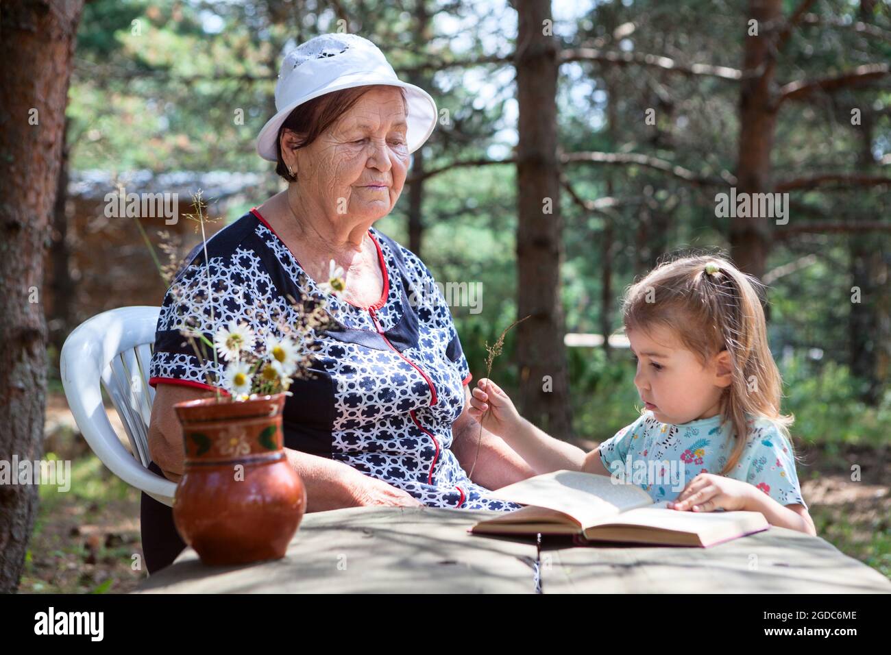 Senior woman play with her granddaughter with cones on wooden table, people living in village Stock Photo