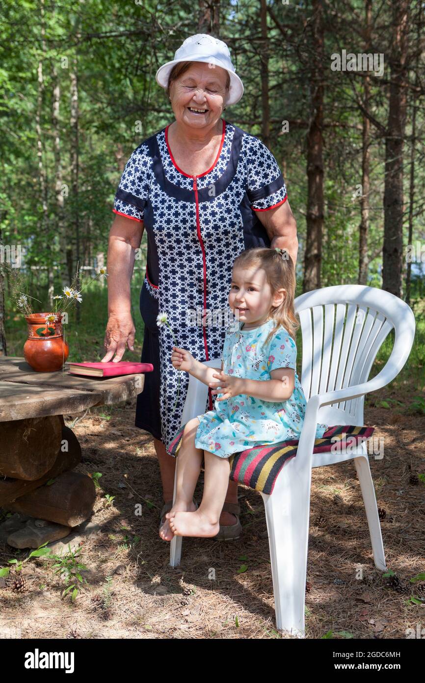 Grandmother spending time with her little granddaughter in summer forest, people sitting together Stock Photo