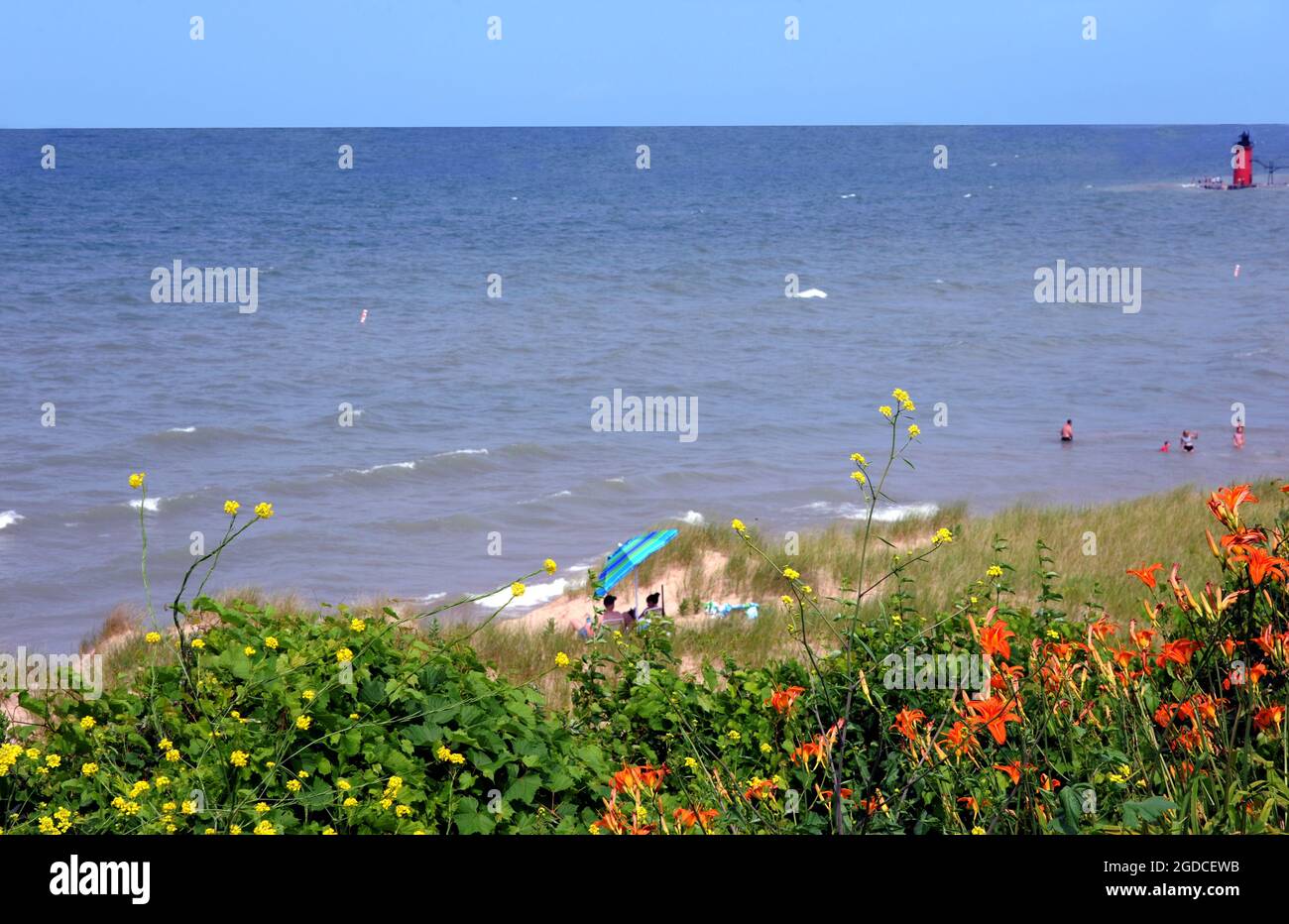 Brightly colored beach umbrellla provides shade on a hot day in July at South Haven, Michigan.  Beach goers enjoy the distant view of the South Haven Stock Photo