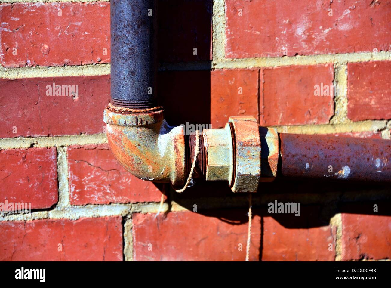 Old brick wall has pipe system running across its surface. Pipe has