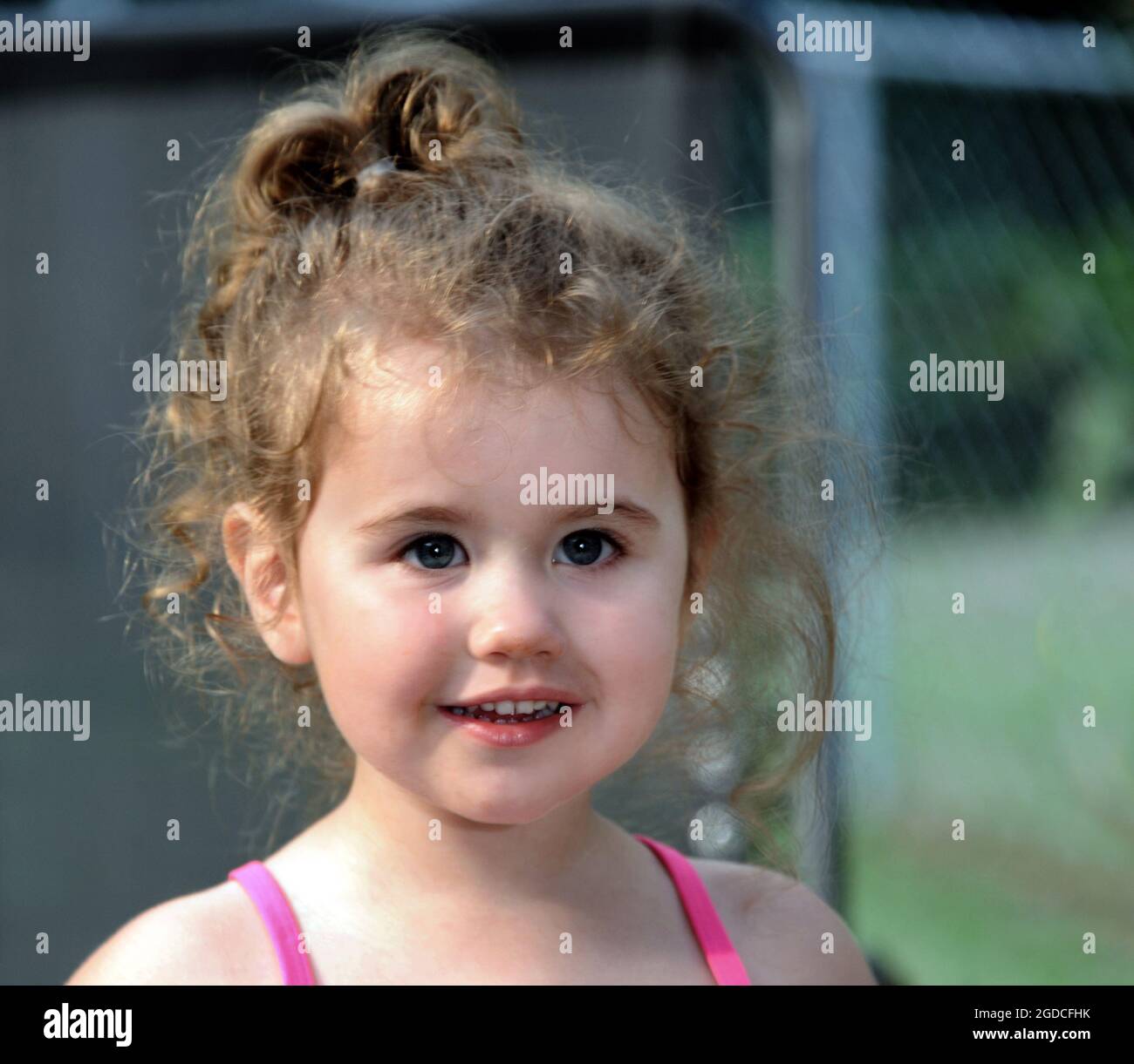 Curls surround little girls head.  Closeup shows the cute twinkle in her eyes.  Pink straps on her shoulders. Stock Photo