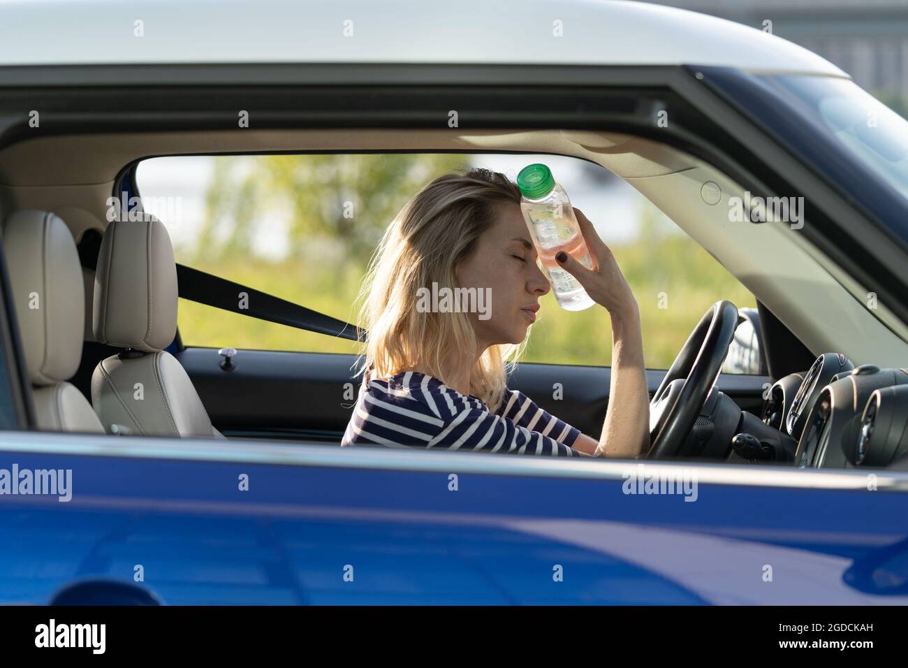 Exhausted girl driver suffering from headache, heat, hot weather applies bottle of water to forehead Stock Photo