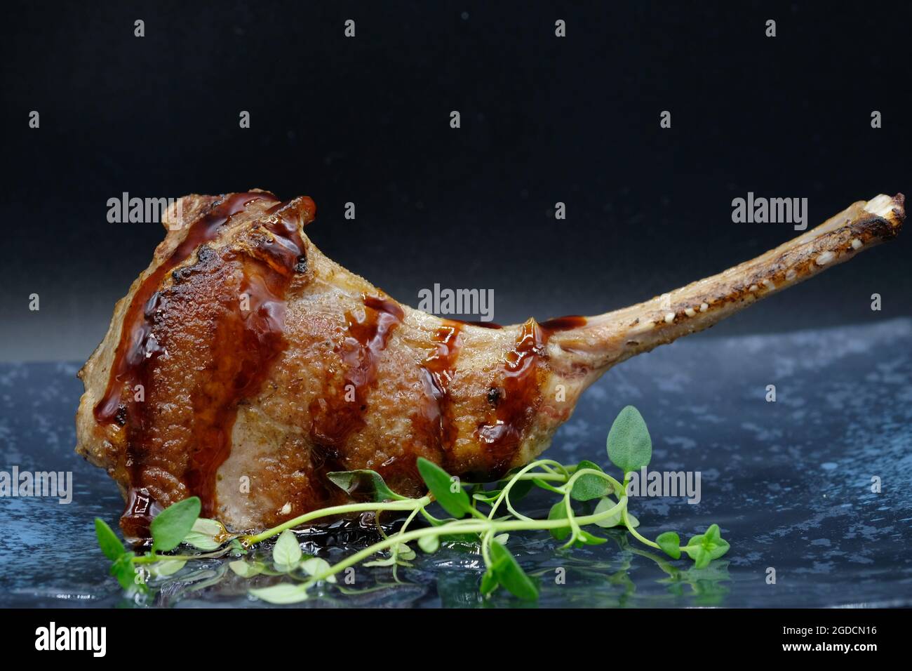 One piece of tasty lamb steak with meat juice served on grey food plate with green vegetable as decoration, with a dark background. Stock Photo