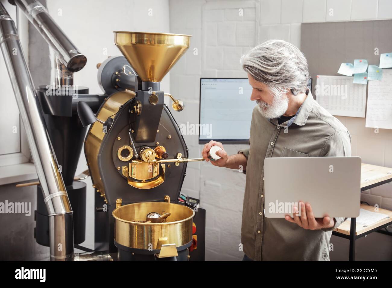 Senior man with laptop using modern coffee roaster Stock Photo