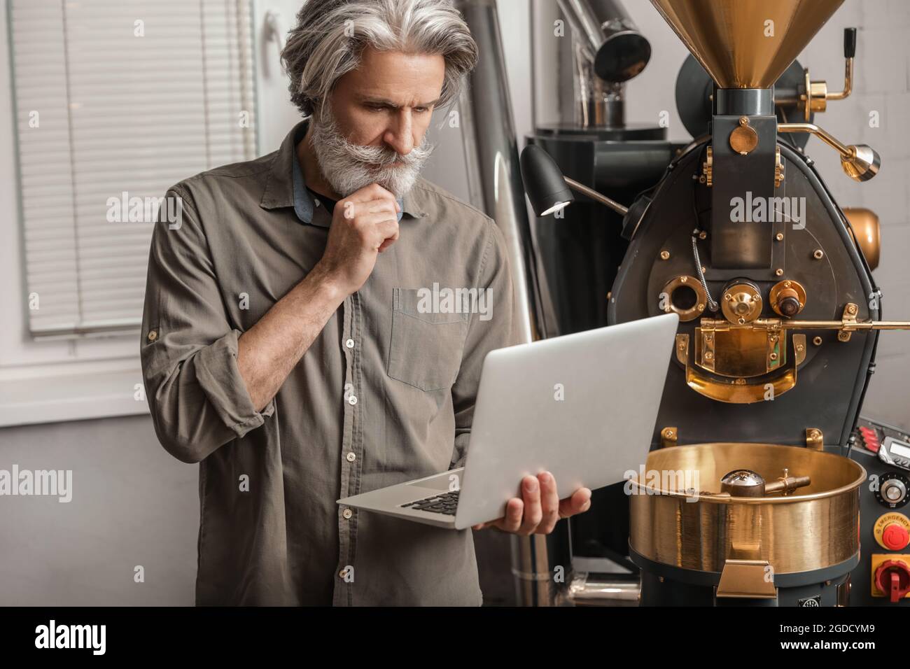 Senior man with laptop using modern coffee roaster Stock Photo