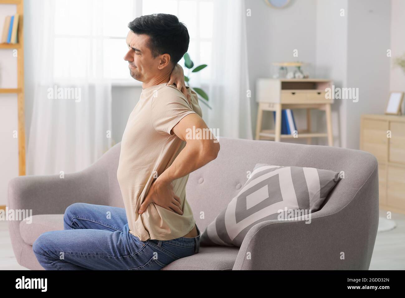 Young man suffering from back pain at home Stock Photo - Alamy