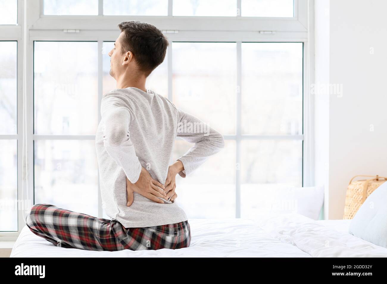 Young man suffering from back pain in bedroom Stock Photo - Alamy