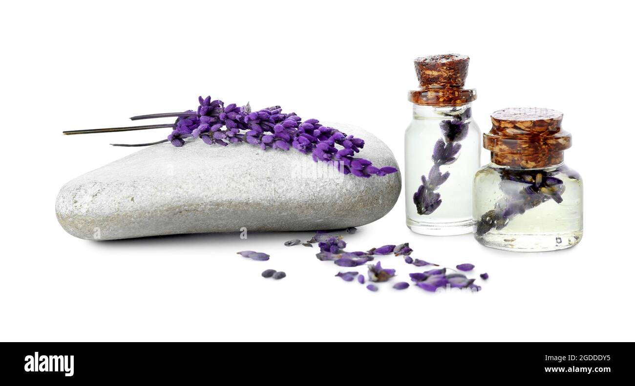 Bottles of lavender essential oil, stone and flowers on white ...