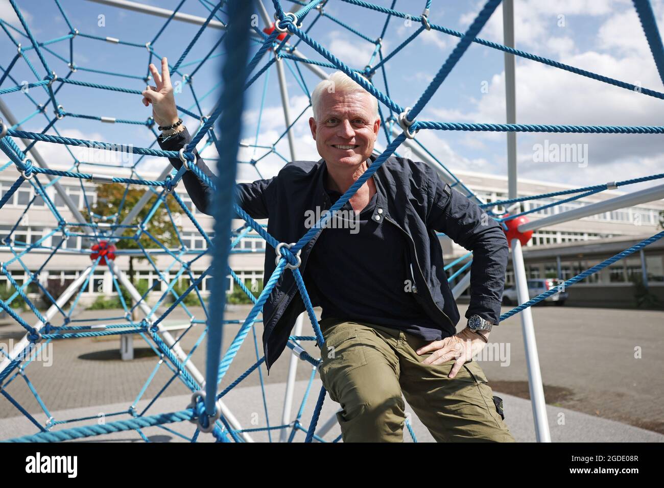 Cologne, Germany. 10th Aug, 2021. Guido Cantz, presenter, sits in a climbing frame in the schoolyard of Dee's Maximilian-Kolbe-Gymnasium. Cantz will be 50 years old on 19.08.2021. (To dpa: 'Rooted between church and sports field - Guido Cantz turns 50') Credit: Oliver Berg/dpa/Alamy Live News Stock Photo