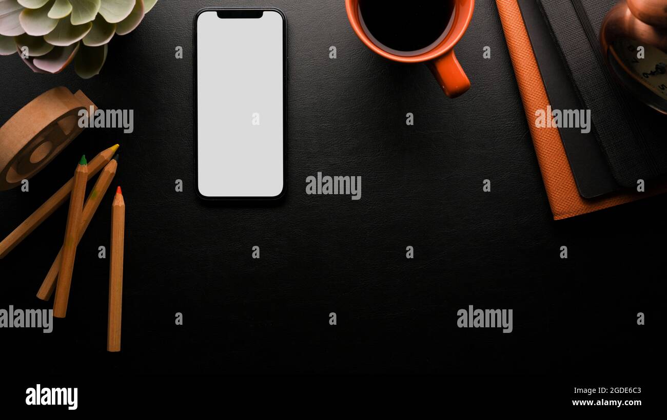 Workspace in black background with copy space, smartphone white screen mockup, black coffee, colour pencils, accessories, Stock Photo