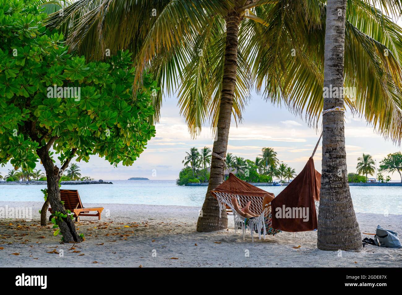 A man relaxing in a hammock under palm trees on a tropical island in the evening Stock Photo