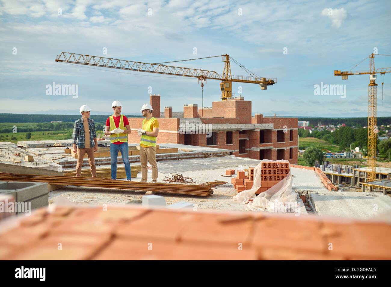 Builders in hardhats conversing with an engineer on the construction site Stock Photo
